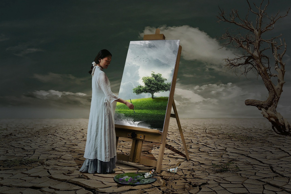 Kobieta stojąca na pustyni przy płótnie  rozstawionym na sztaludze malarskiej